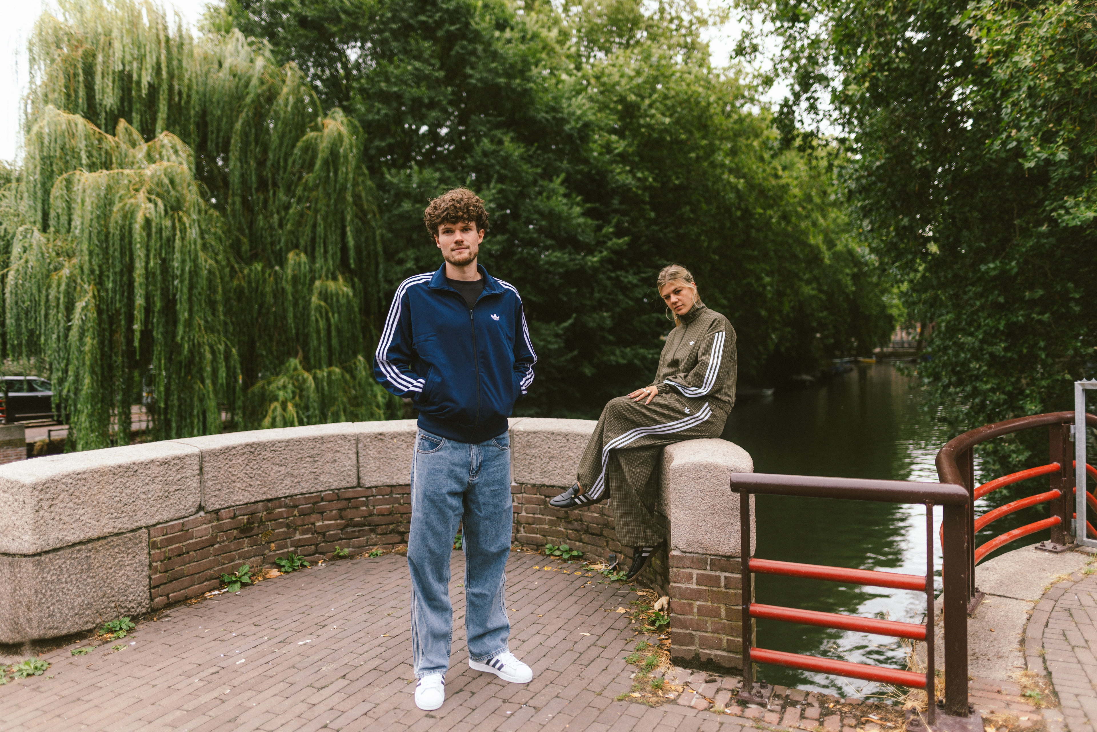 Twee modellen die poseren op een brug in adidas kleding en schoeisel.